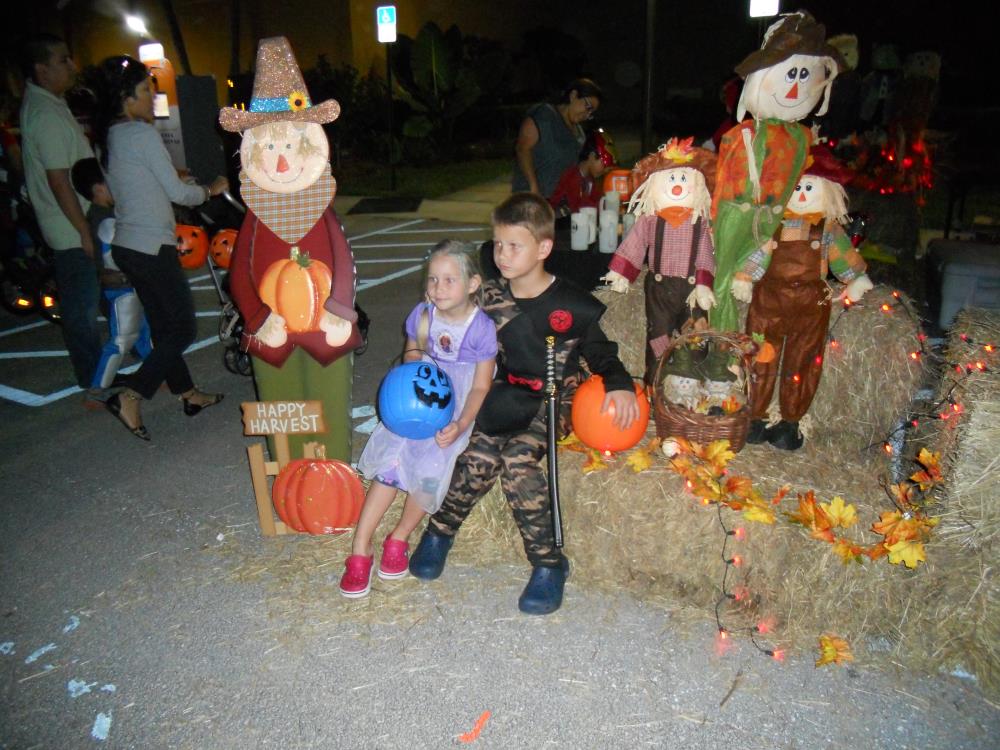 Girl in purple princess outfit and blue jack-o-lantern bucket sitting on hay bales next to boy in black and camouflage ninja outfit